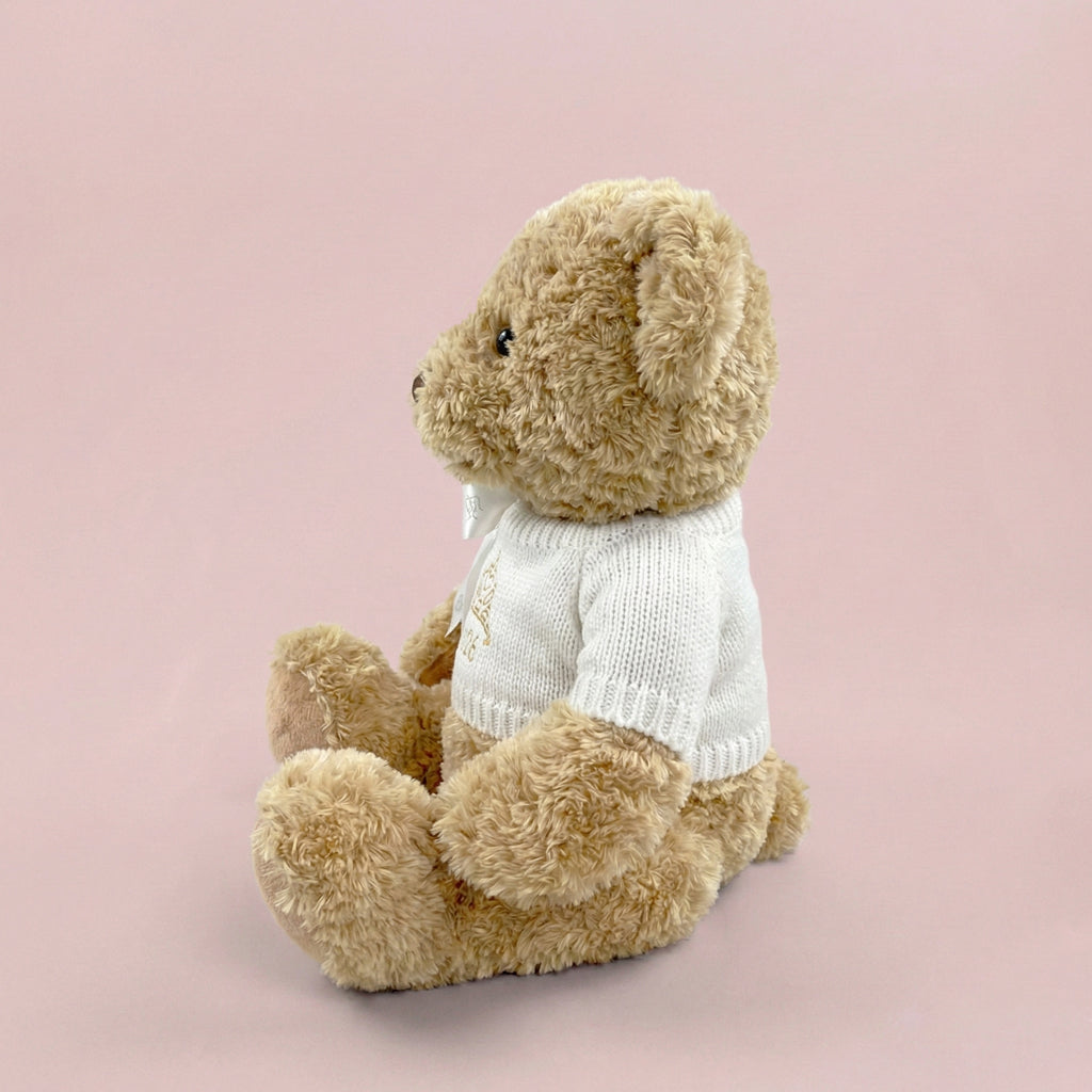 A traditional style seated teddy bear with a white knitted jumper embroidered with a crown or tiara design and the year 2026 in gold thread.